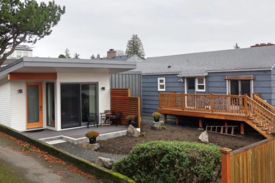 White accessory dwelling unit in backyard of small grey home in Seattle, Washington.